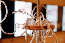 Wooden disk with tubes hanging off of it.
A metal rod passes through the middle. In the background, blurred, are two monitors with a human figure.