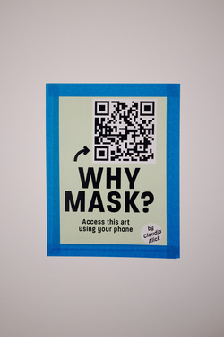 A printed sign taped to a white wall at the entrance to the E.A.A.T. exhibition . The sign has a light green background and features a large, bold title in black text: "WHY MASK?" Below the title, smaller black text reads: "Access this art using your phone." Above the title, there is a QR code, accompanied by a small curved arrow pointing to it, indicating that scanning it will provide access to the artwork. In the bottom right corner, there is a circular label with black text that reads: "by Claudia Alick".The sign is neatly taped, with the blue tape forming a frame around its edges.