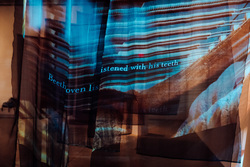 Projected in white onto translucent black fabric, the words “Beethoven listened with his teeth” are written against a blurry image of a piano.
