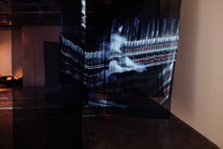 Piano hammers and a blurry image of a piano player are projected in white onto translucent black fabric.