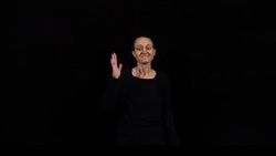 A person standing against a black background with one hand raised in a waving gesture and a friendly expression on their face. They are wearing a black long-sleeved shirt.