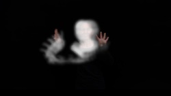 Blurred image of a person with raised hands against a black background, creating a ghostly effect.